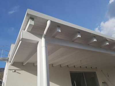 Vista frontale di una tettoia in legno lamellare Abete impregnata bianco con copertura finale in alluminio aggraffato complete di gronde e accessori, realizzata a Trapani (TP).